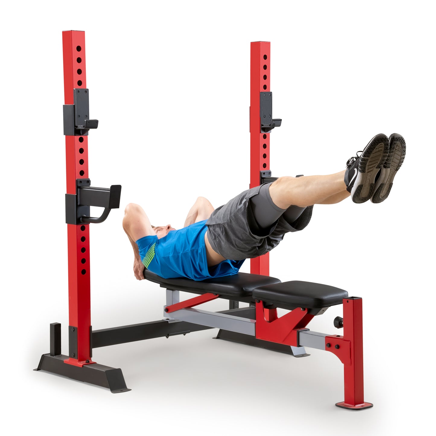 Man performing a lying leg raise exercise on the flat setting of the red and black adjustable weight bench rack system.